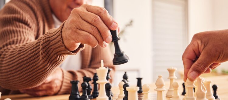 A man sits at a desk moving a chess piece during a game.