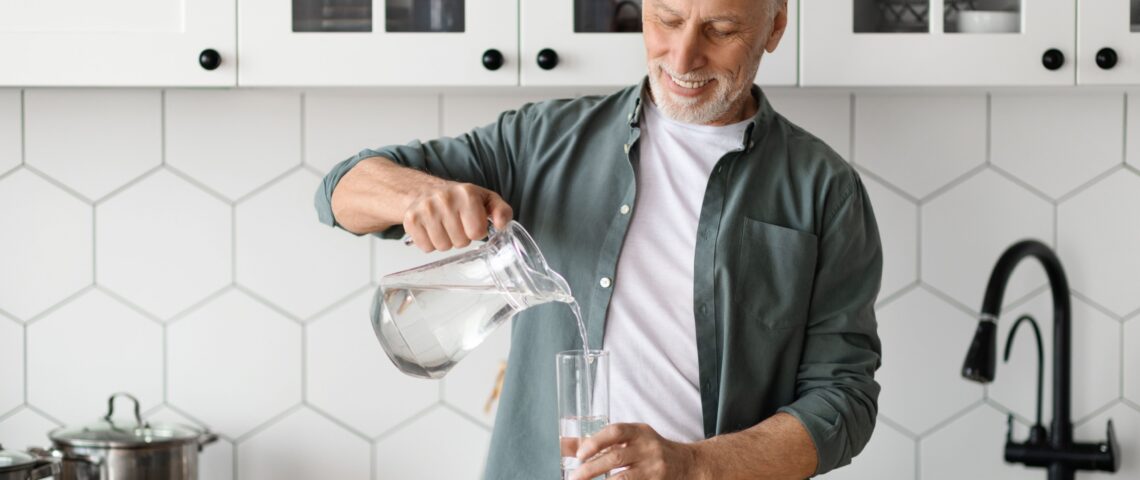 A man pours a glass of water from a jug in his kitchen.