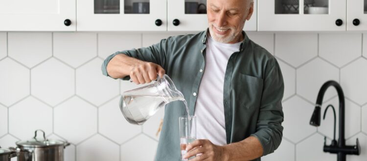 A man pours a glass of water from a jug in his kitchen.