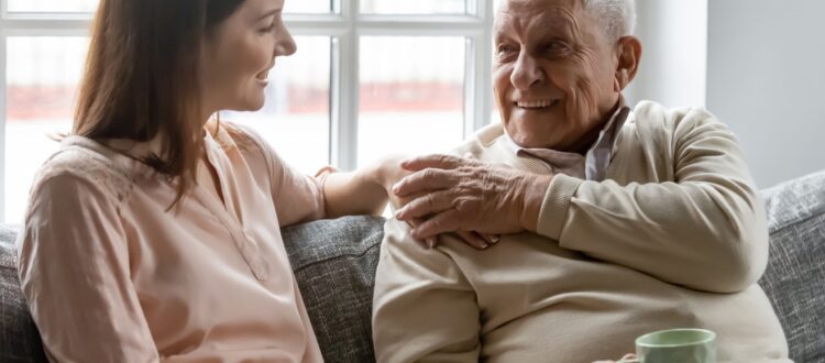 A young woman and her grandfather have a cup of tea on the sofa