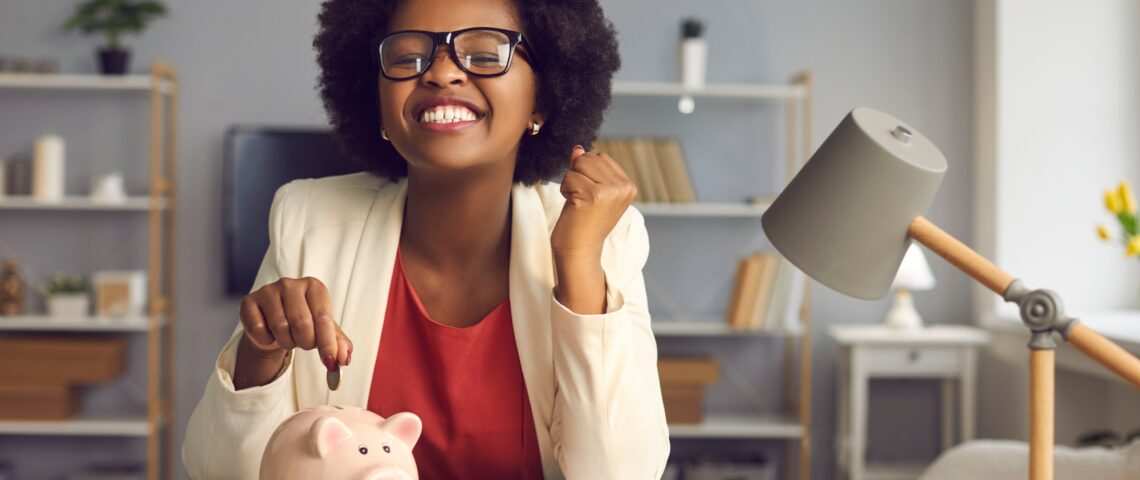 Excited woman sitting at a desk putting a coin into a piggybank