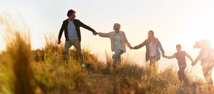 A multi-generational family walking hand in hand across a field at sunset