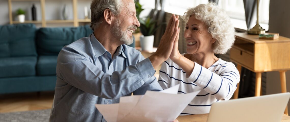 Excited older couple giving each other a high five while doing paperwork