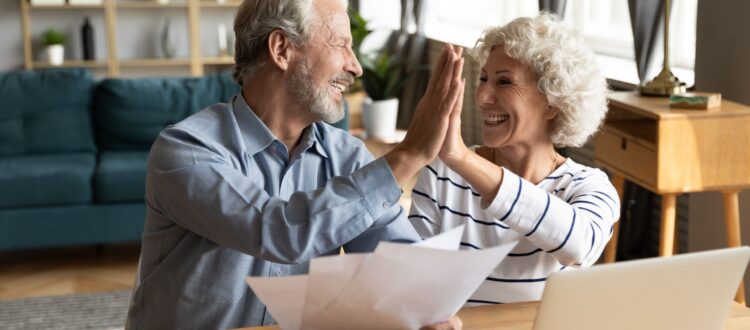 Excited older couple giving each other a high five while doing paperwork