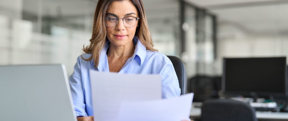 Woman sitting at a desk with a laptop compares documents