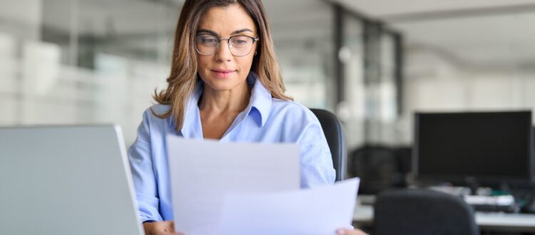 Woman sitting at a desk with a laptop compares documents