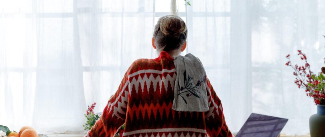 Woman alone in a red Christmas jumper stands in front of a laptop