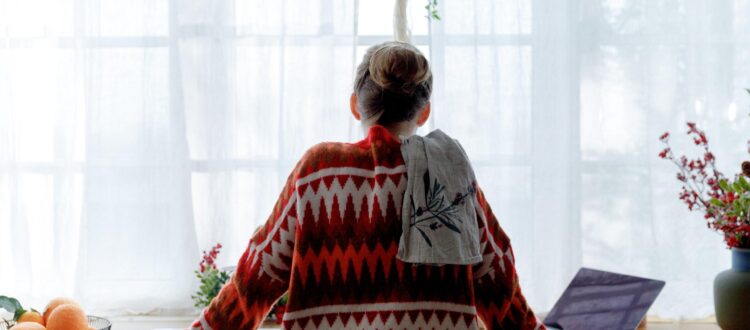 Woman alone in a red Christmas jumper stands in front of a laptop