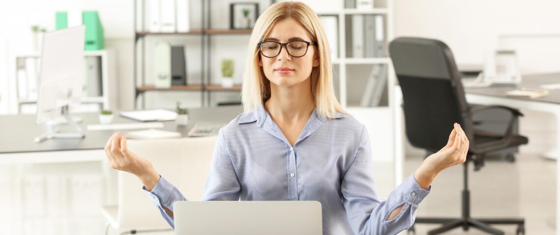 Woman meditating at her desk with a laptop and notebooks
