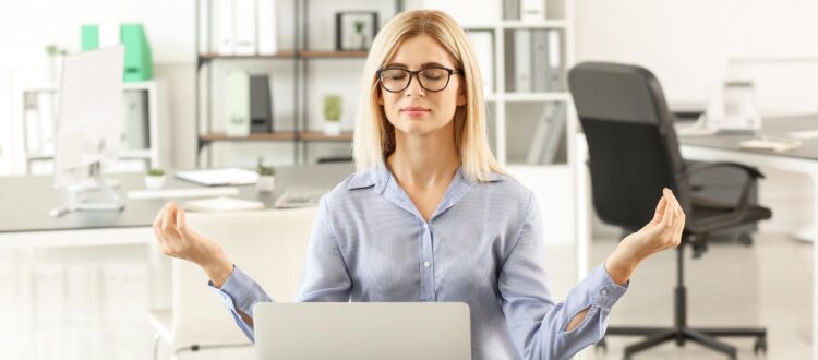 Woman meditating at her desk with a laptop and notebooks