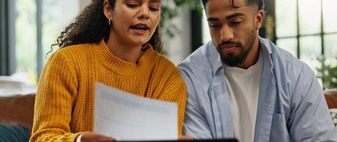 Couple talking at home while looking at a document in front of laptop