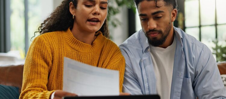 Couple talking at home while looking at a document in front of laptop